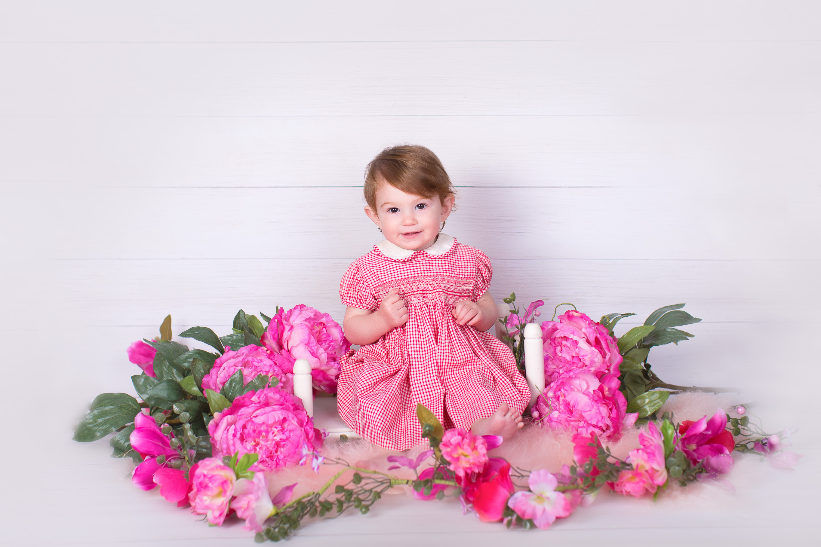 Image of little girl in pink dress posing for first birthday session with pink flowers around her