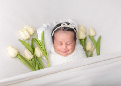 Newborn baby sleeping surrounded by white tulips