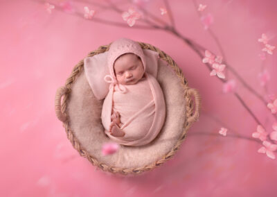 Newborn baby wrapped up and wearing a hat on pink backdrop