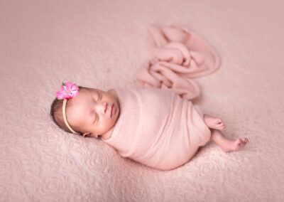 Baby girl sleeping wrapped up on pink backdrop