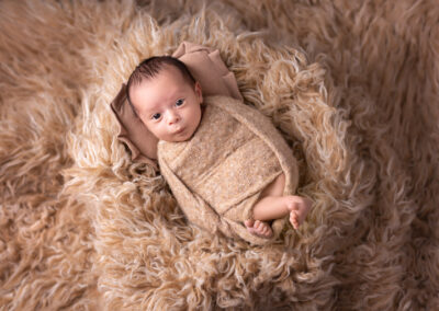 Awake newborn baby posed on fur rug