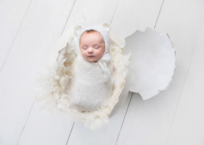 Baby wearing bear hat and posed in egg shell